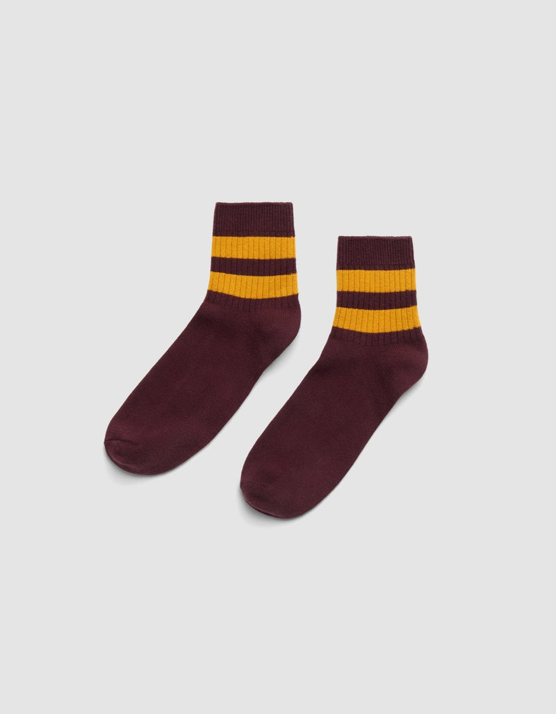 The Women's Sadie Sock by Cozy Earth is shown in maroon with two thick yellow stripes near the top, set against a plain white background.