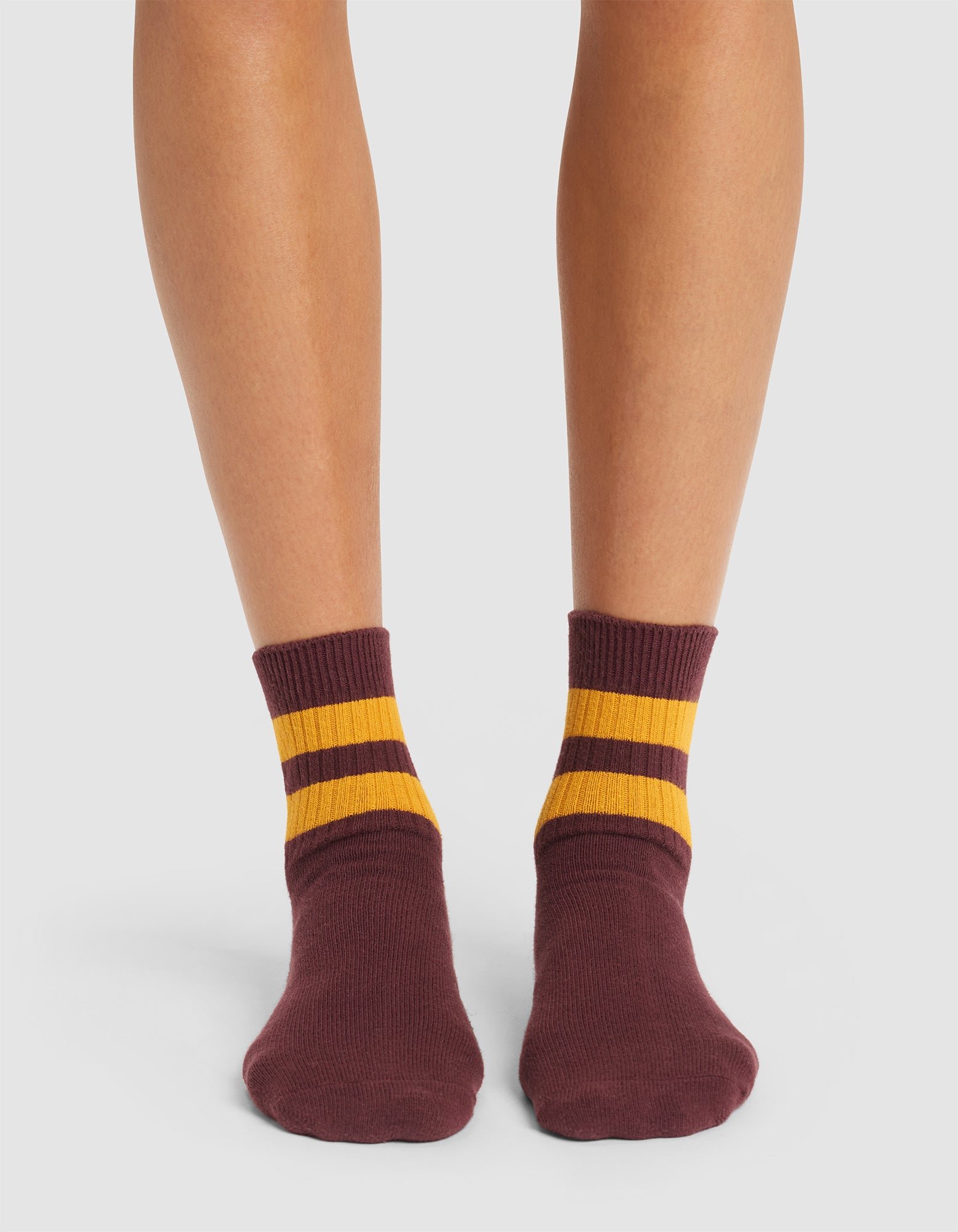 A pair of feet wearing Cozy Earth Women's Sadie Socks, maroon with two yellow stripes at the top, standing on a white background.  