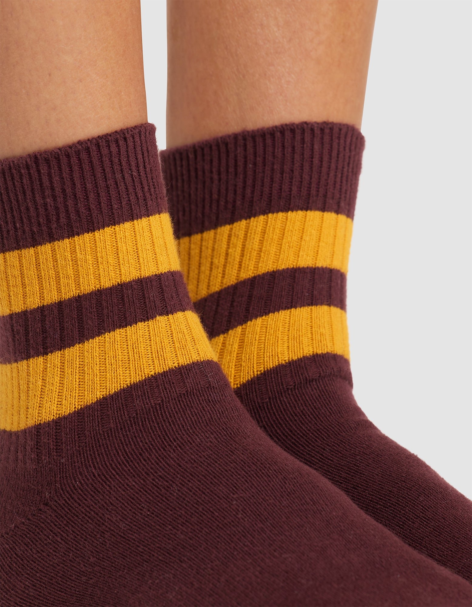 Close-up of feet wearing Cozy Earth Women's Sadie Sock in maroon, featuring thick yellow and maroon ankle stripes. The background is plain and light-colored. 