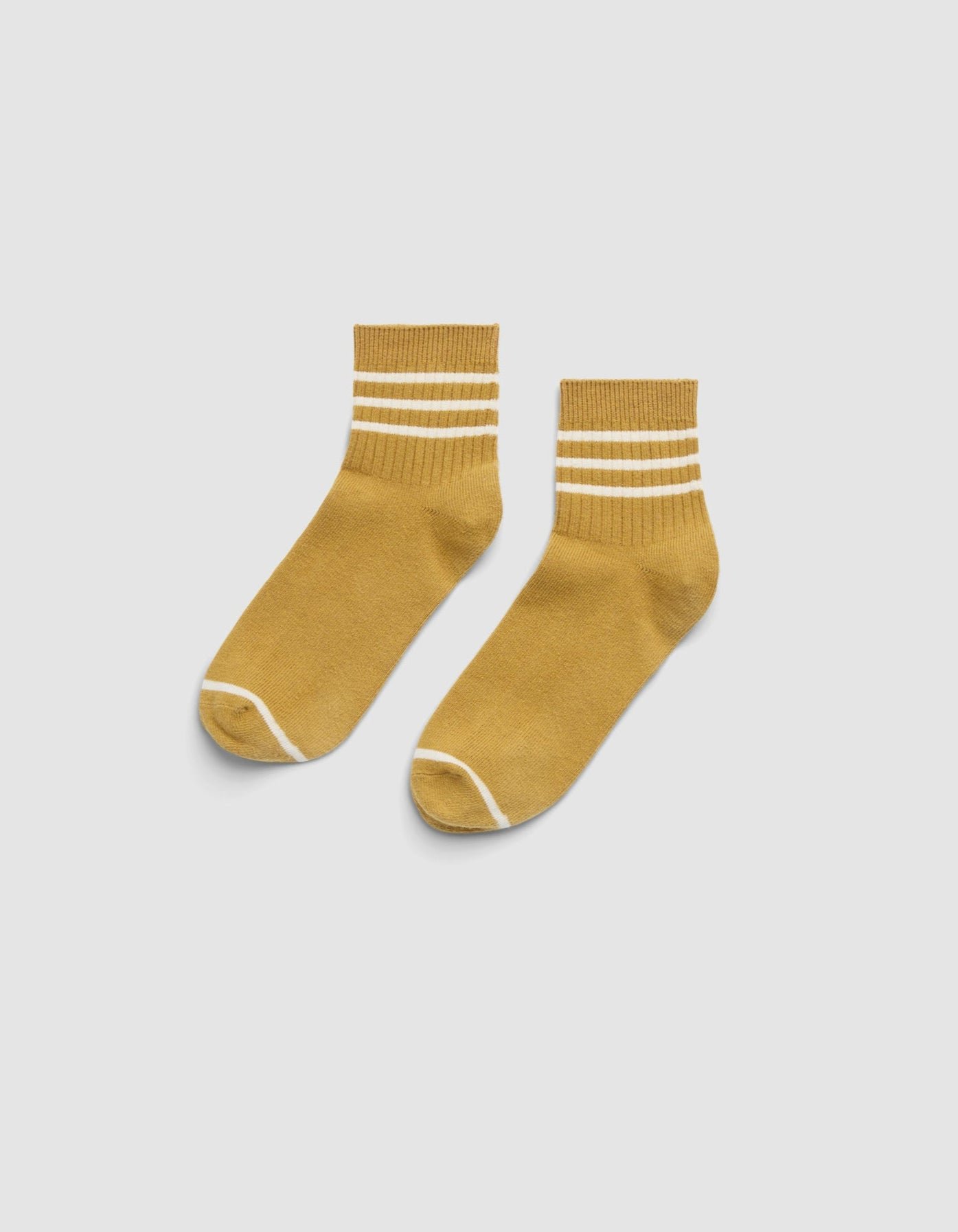 The Cozy Earth Women's Sadie Sock is a mustard yellow ankle sock with two white stripes near the top and white trim at the toe and heel, shown on a light gray background. 