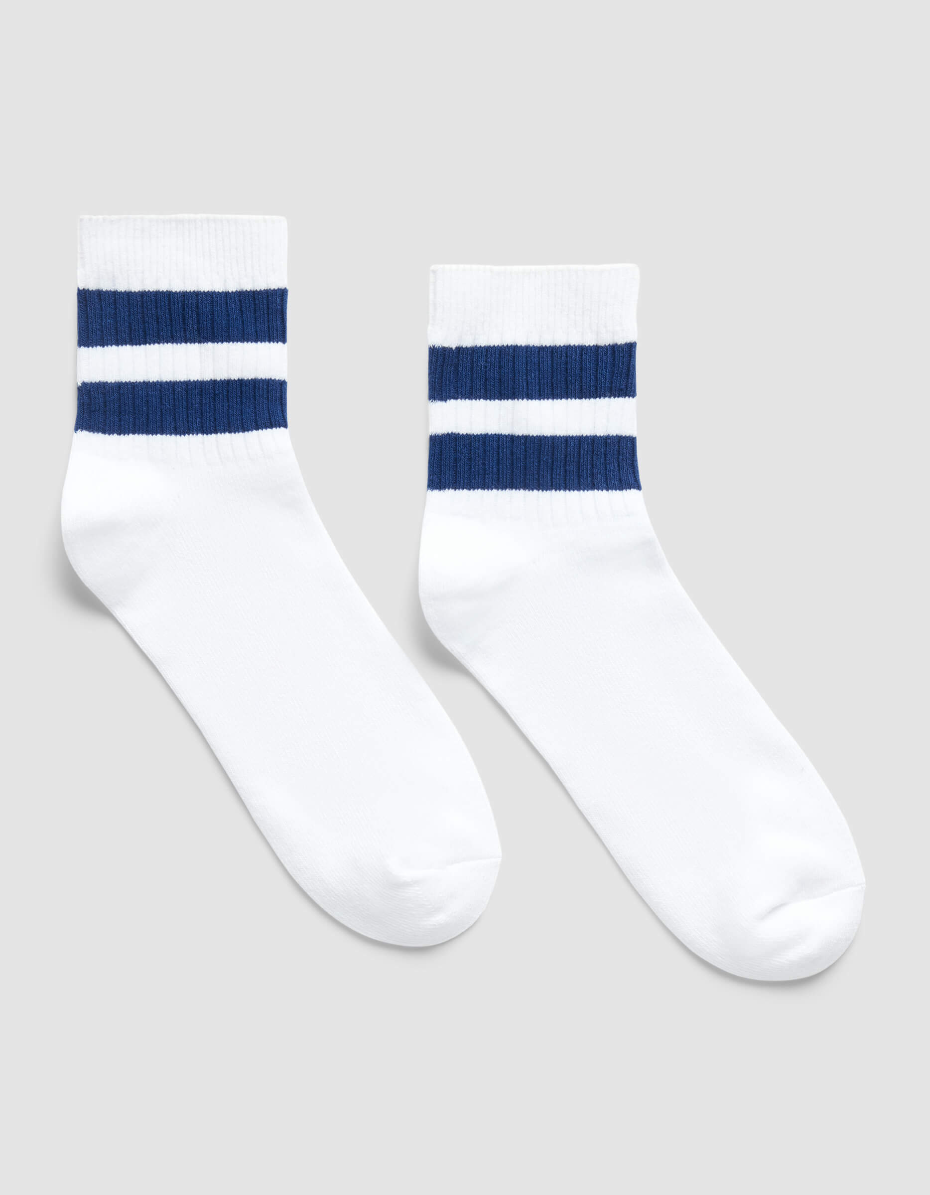 The Women's Sadie Sock by Cozy Earth is a white crew sock featuring two horizontal navy blue stripes near the top, shown on a light gray background.