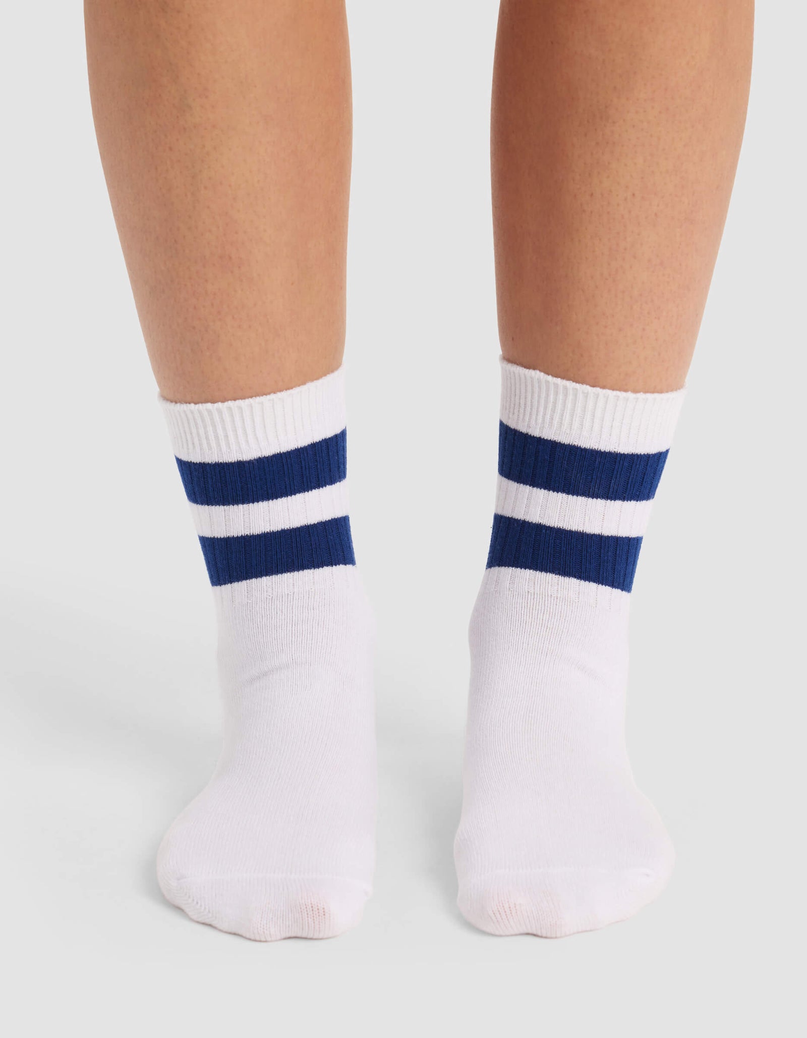 A person models Cozy Earth's Women's Sadie Sock, featuring two navy blue stripes near the top, while standing on a light gray surface.