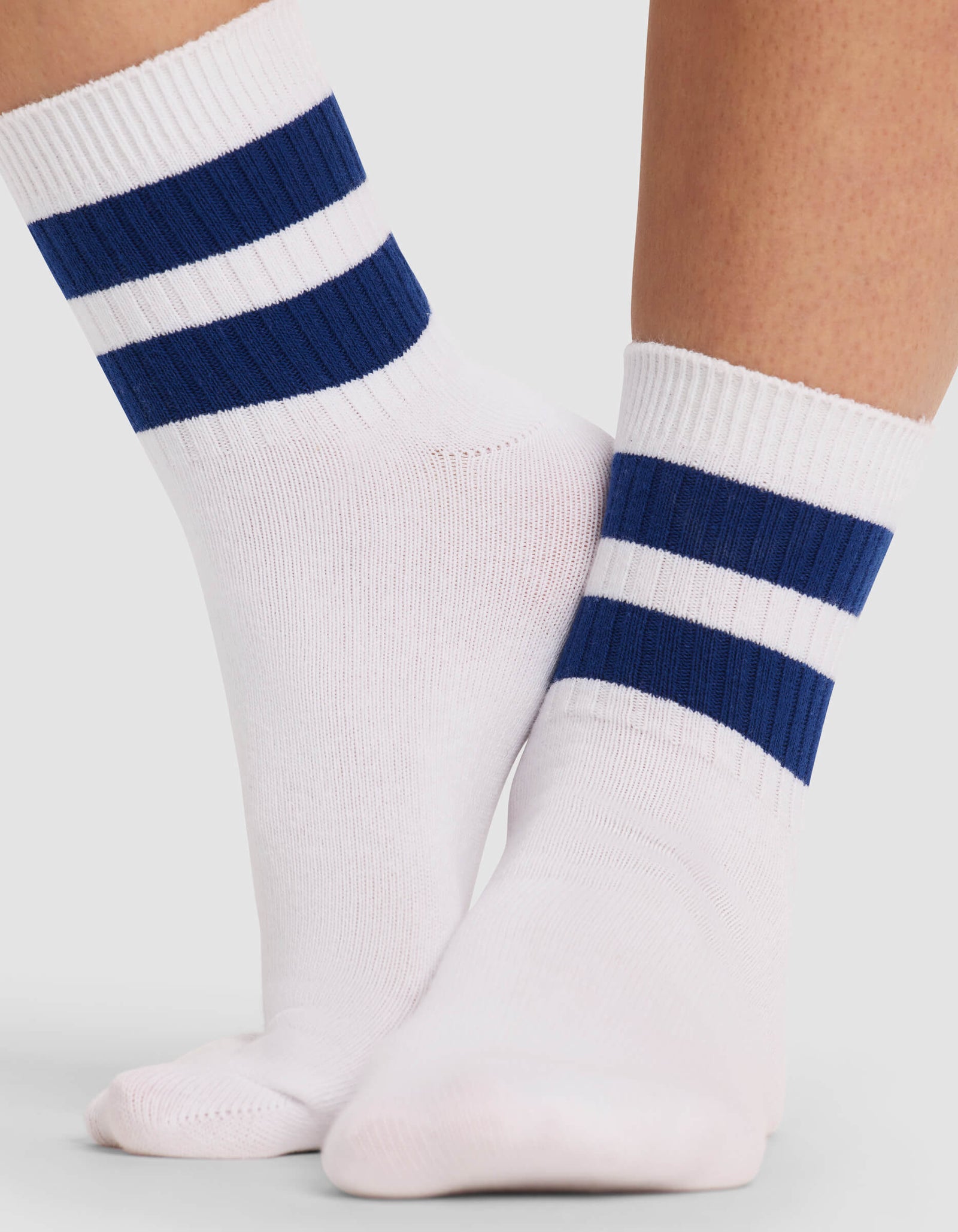 A close-up of two feet wearing Cozy Earth Women's Sadie Socks—white crew socks featuring two thick navy blue stripes near the top—set against a plain light background.