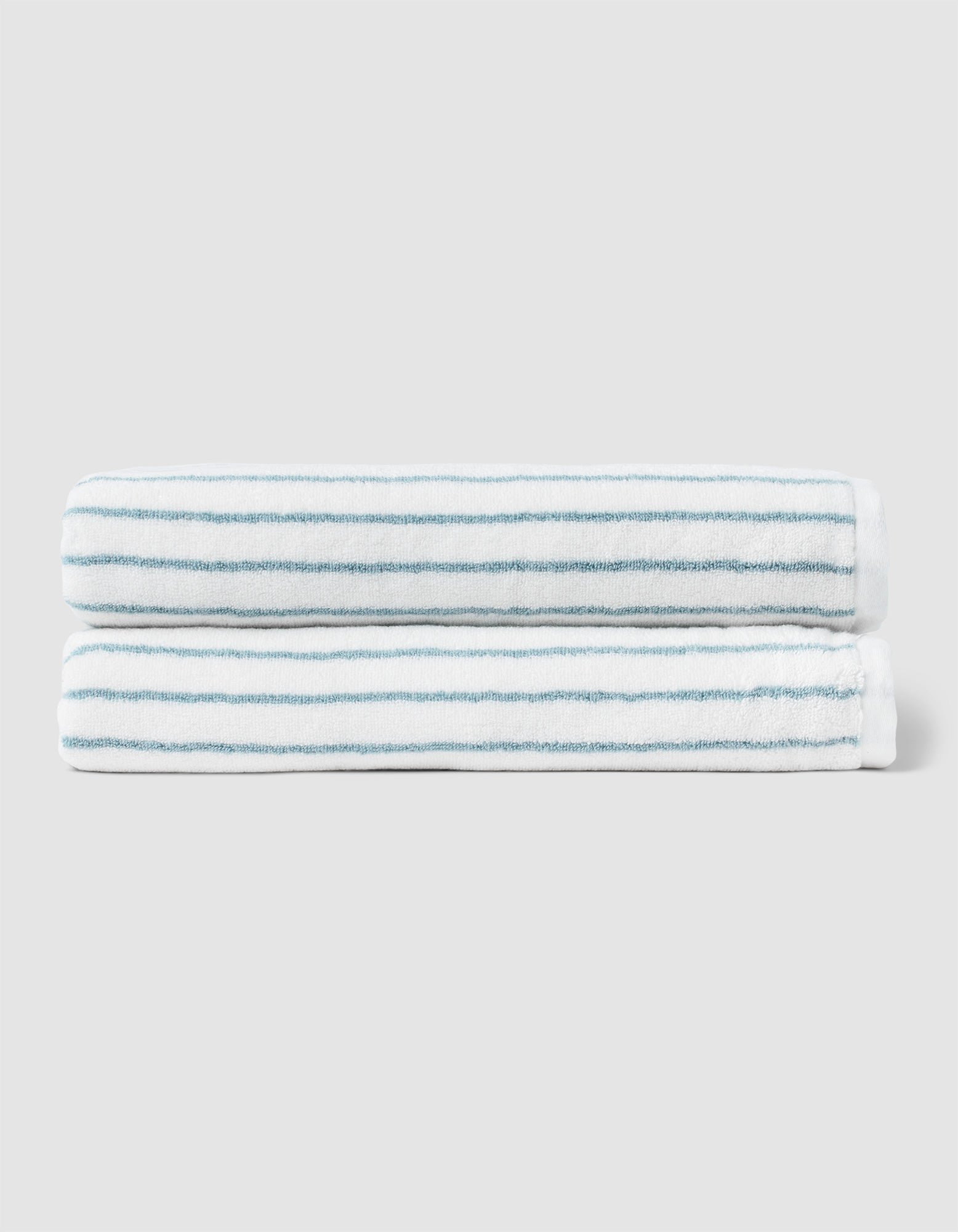 Two neatly folded Cozy Earth Striped Luxe Bath Sheets, featuring thin light blue stripes, are stacked together against a plain light gray background. |Color:Brook Stripe