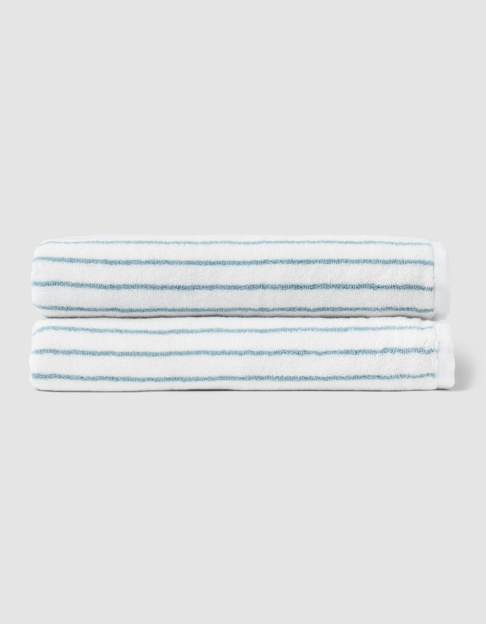 Two neatly folded Cozy Earth Striped Luxe Bath Sheets, featuring thin light blue stripes, are stacked together against a plain light gray background. 