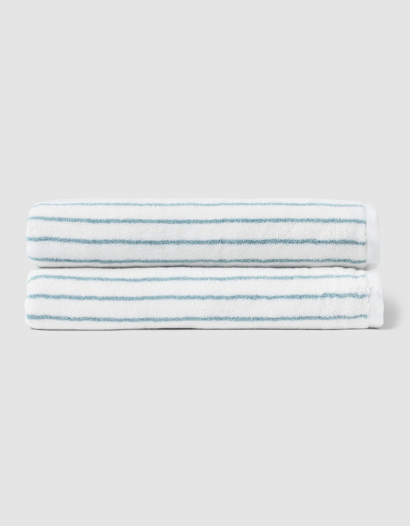 Two neatly folded Cozy Earth Striped Luxe Bath Sheets, featuring thin light blue stripes, are stacked together against a plain light gray background.