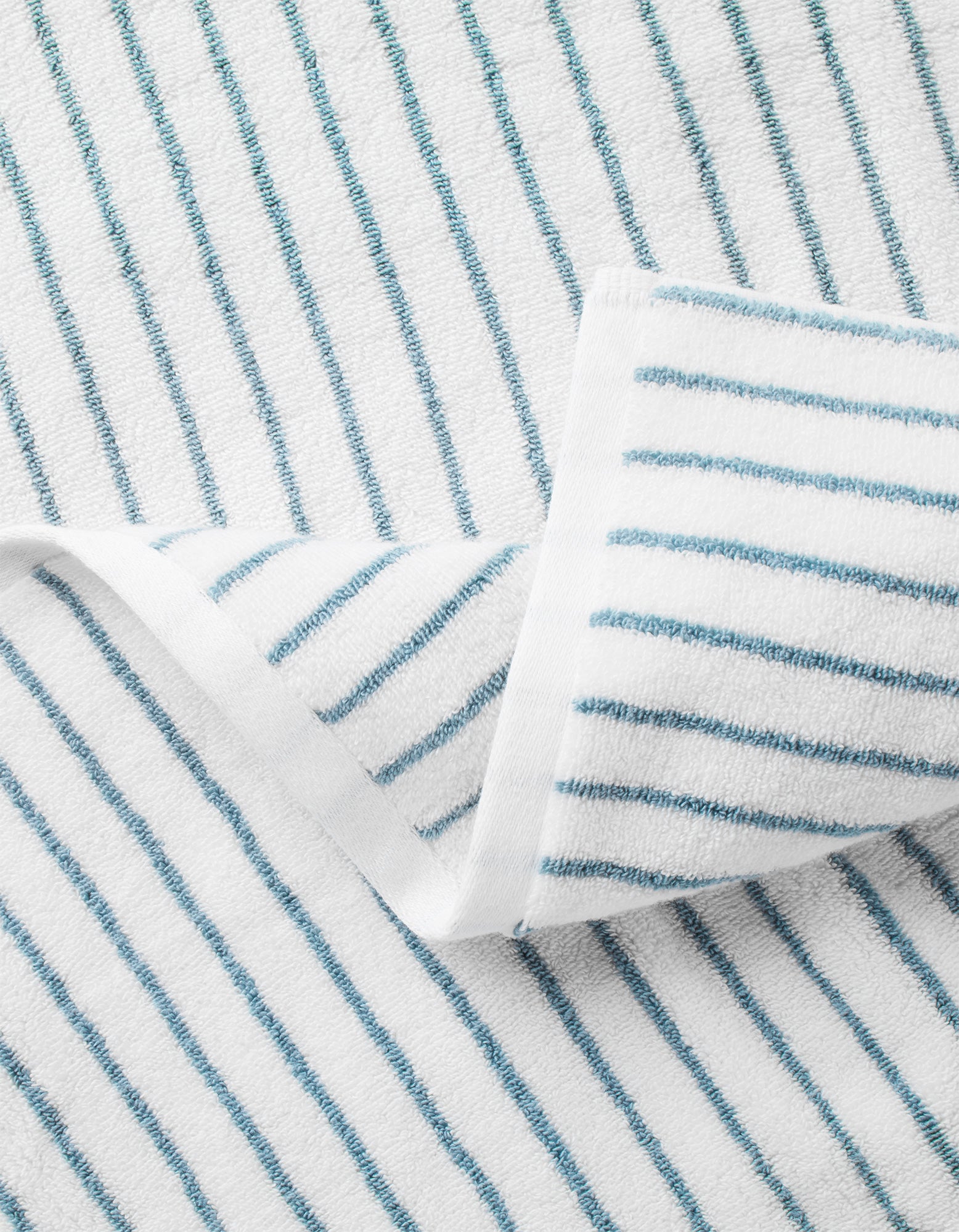 A close-up of Cozy Earth's Striped Luxe Bath Sheets in white with thin blue diagonal stripes, featuring a folded corner to highlight the textured detail. 