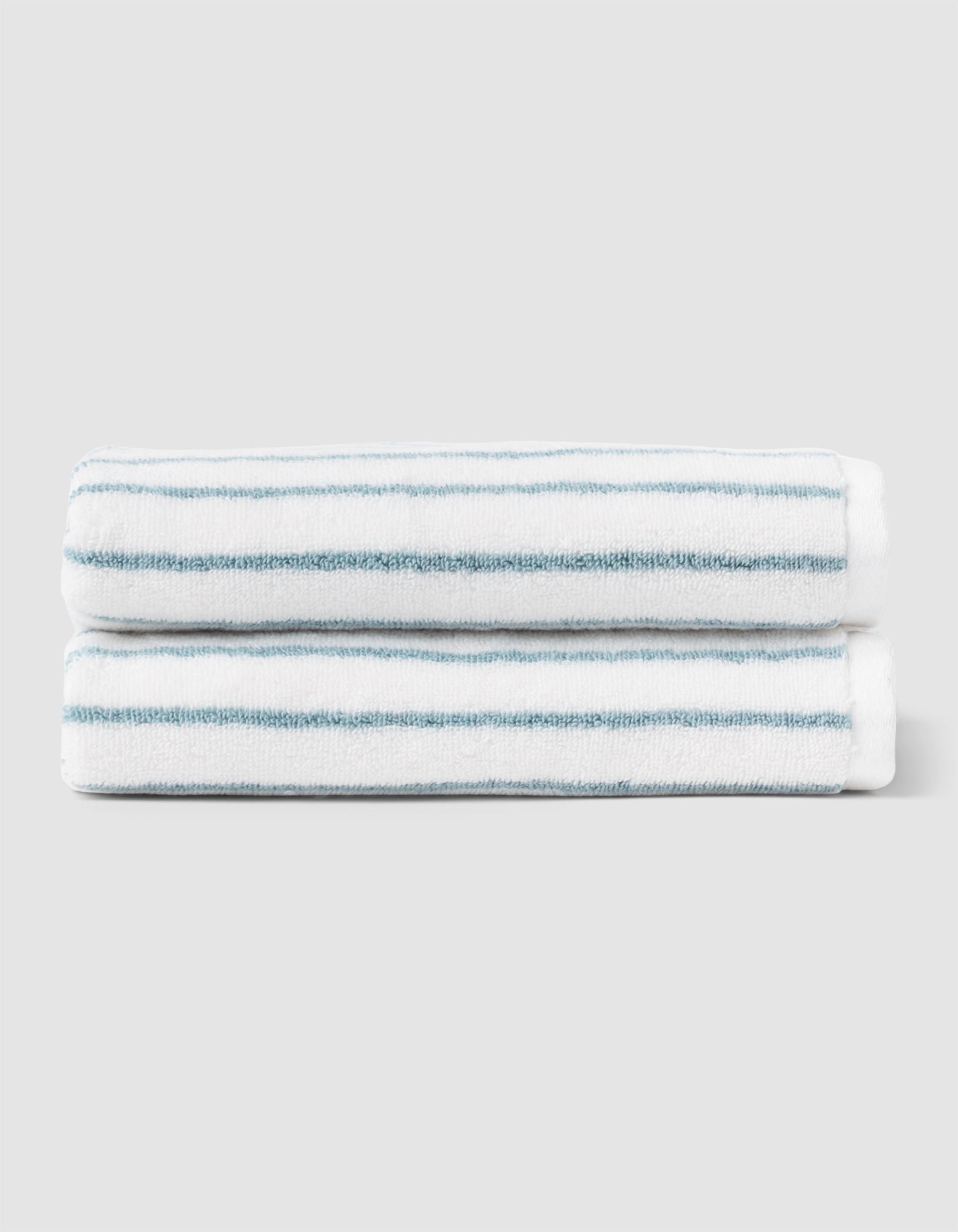 Two Striped Luxe Hand Towels by Cozy Earth, featuring thin teal horizontal stripes on white, are neatly folded and stacked against a light gray background. |Color:Brook Stripe