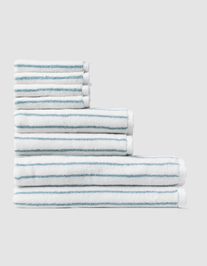 The Striped Luxe Bath Towel Set by Cozy Earth, featuring thin blue stripes on white towels, is neatly arranged in a stepped formation against a plain light gray background.