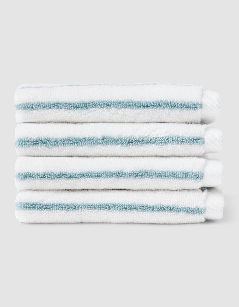Five Striped Luxe Washcloths by Cozy Earth, white with light blue stripes, are neatly stacked against a plain light gray background.