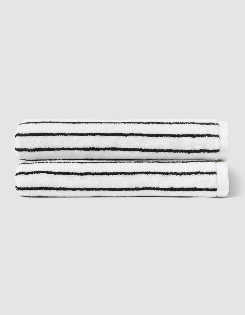 Two neatly folded Striped Luxe Bath Towels by Cozy Earth, featuring horizontal black stripes on white, are stacked together against a light gray background.