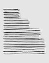 The Complete Striped Luxe Bath Bundle by Cozy Earth features neatly stacked white towels with thin black stripes, arranged in descending size order on a light gray background. |Color:Black Stripe