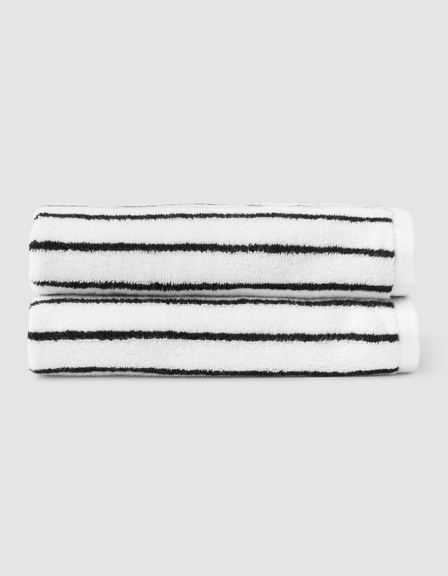 Two Cozy Earth Striped Luxe Hand Towels with black horizontal stripes are neatly stacked against a plain light gray background. 