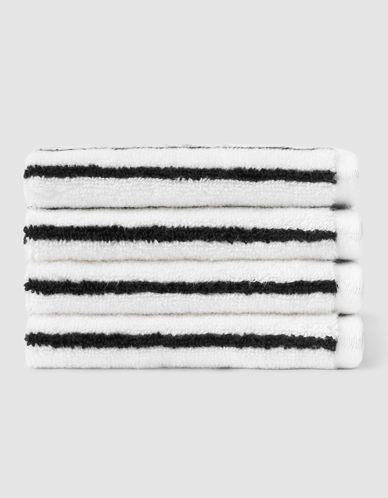 A stack of four neatly folded Cozy Earth Striped Luxe Washcloths in white with evenly spaced black stripes, set against a plain light gray background. 