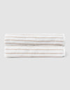 Two Striped Luxe Bath Sheets by Cozy Earth, featuring white fabric with thin, evenly spaced tan stripes, are neatly folded and stacked against a plain light gray background.  |Color:Sand Stripe