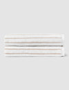 Two Striped Luxe Bath Towels by Cozy Earth, featuring thin light brown stripes on white, are stacked neatly against a plain light gray background. |Color:Sand Stripe