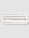 Two Striped Luxe Hand Towels by Cozy Earth, in white with light brown stripes, are neatly folded and stacked against a plain light gray background. |Color:Sand Stripe