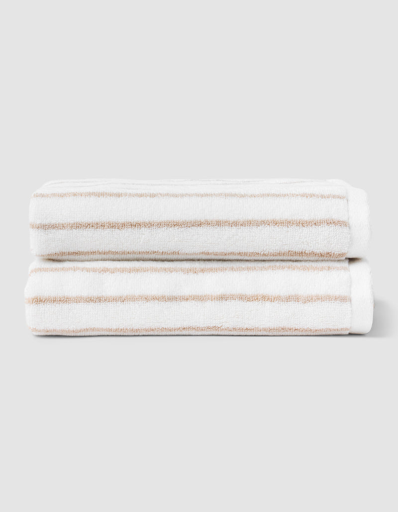 Two Striped Luxe Hand Towels by Cozy Earth, in white with light brown stripes, are neatly folded and stacked against a plain light gray background.