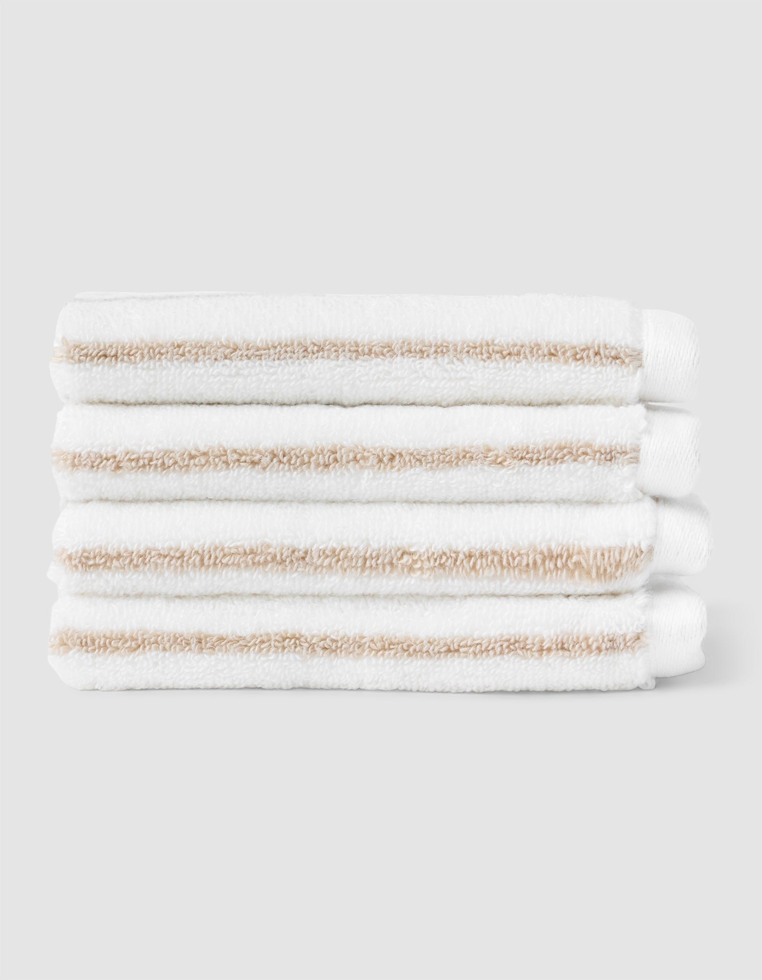 Four Cozy Earth Striped Luxe Washcloths, featuring white fabric with light beige stripes, are stacked neatly against a plain light gray background. |Color:Sand Stripe