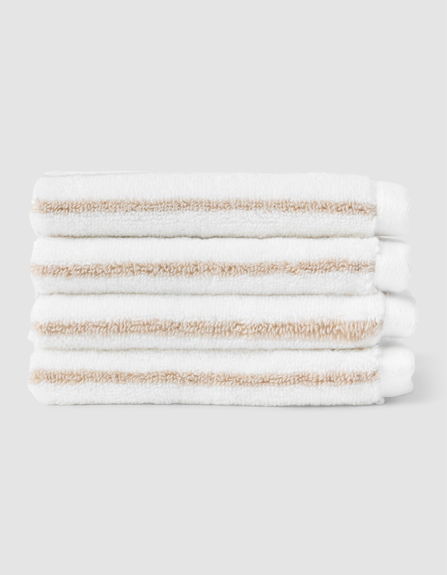 Four Cozy Earth Striped Luxe Washcloths, featuring white fabric with light beige stripes, are stacked neatly against a plain light gray background. 