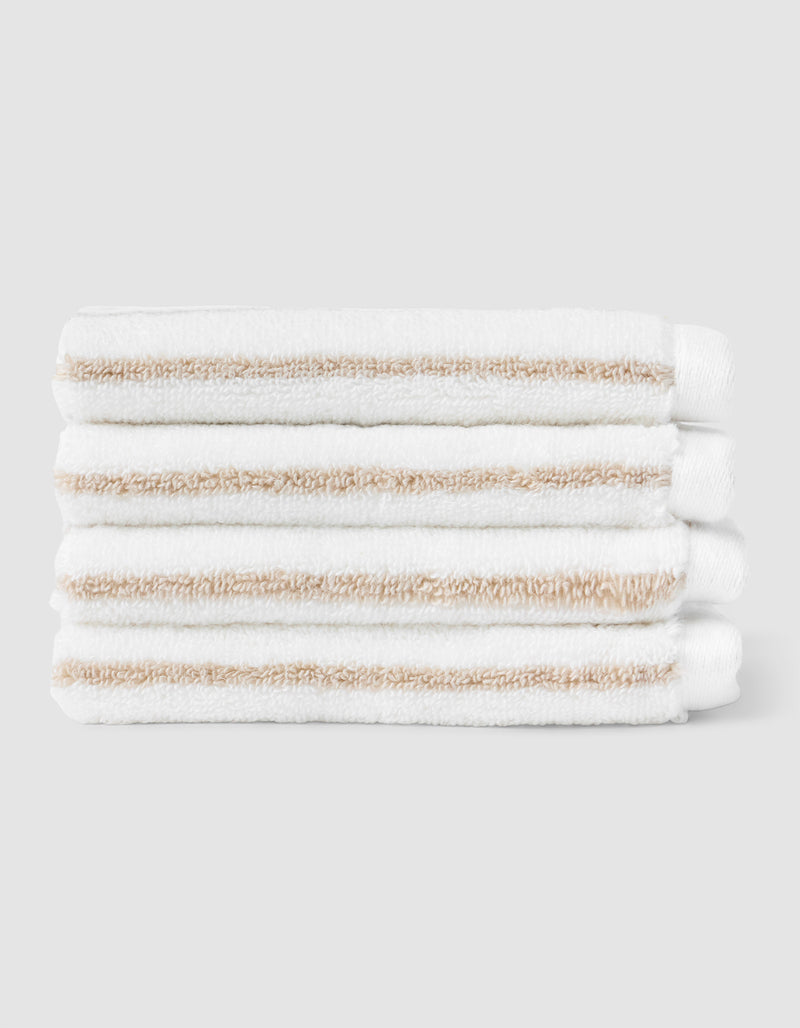 Four Cozy Earth Striped Luxe Washcloths, featuring white fabric with light beige stripes, are stacked neatly against a plain light gray background.
