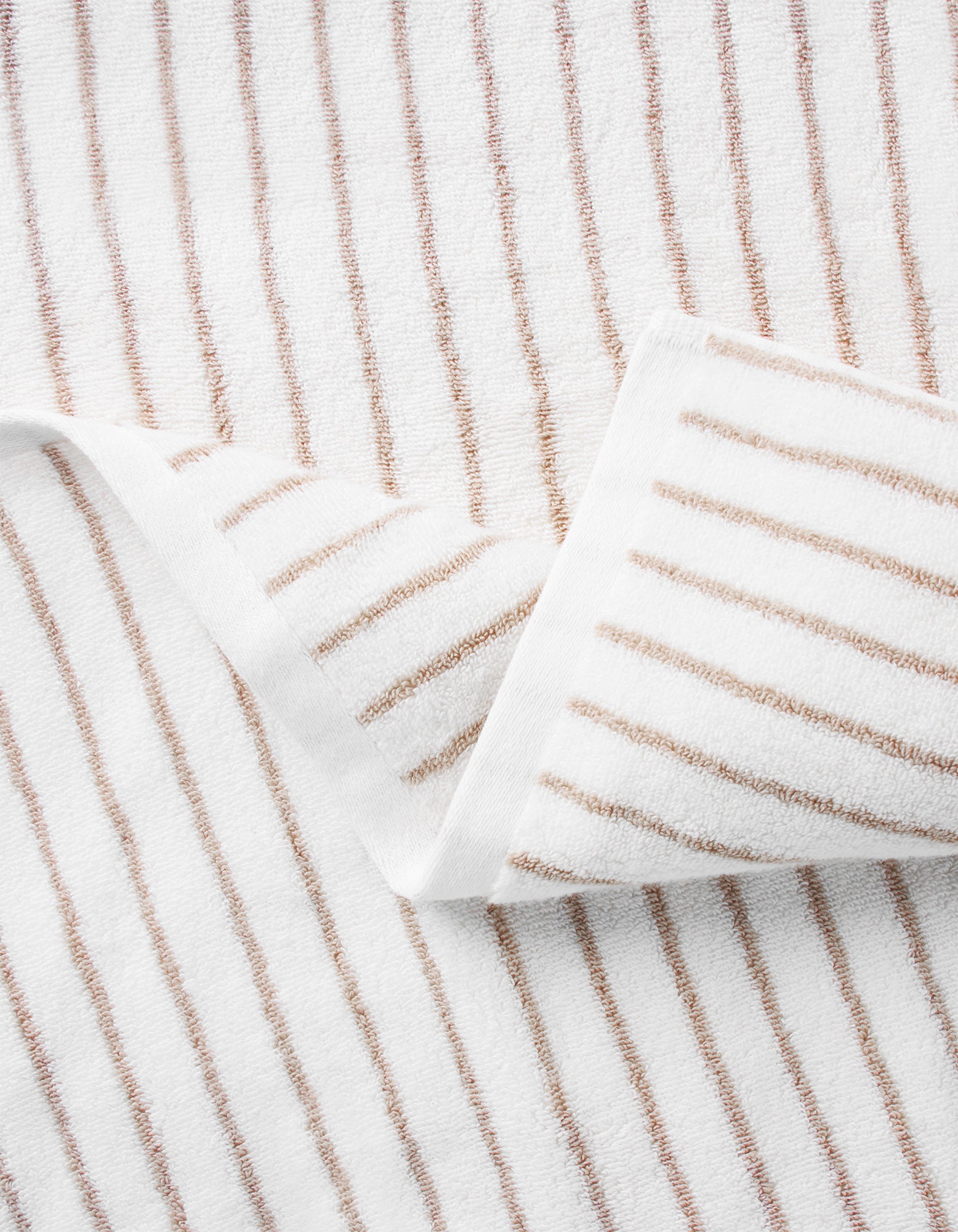 A close-up of Cozy Earth's Striped Luxe Washcloths shows evenly spaced brown stripes on white fabric, with one corner folded to display the signature striped pattern on both sides. |Color:Sand Stripe