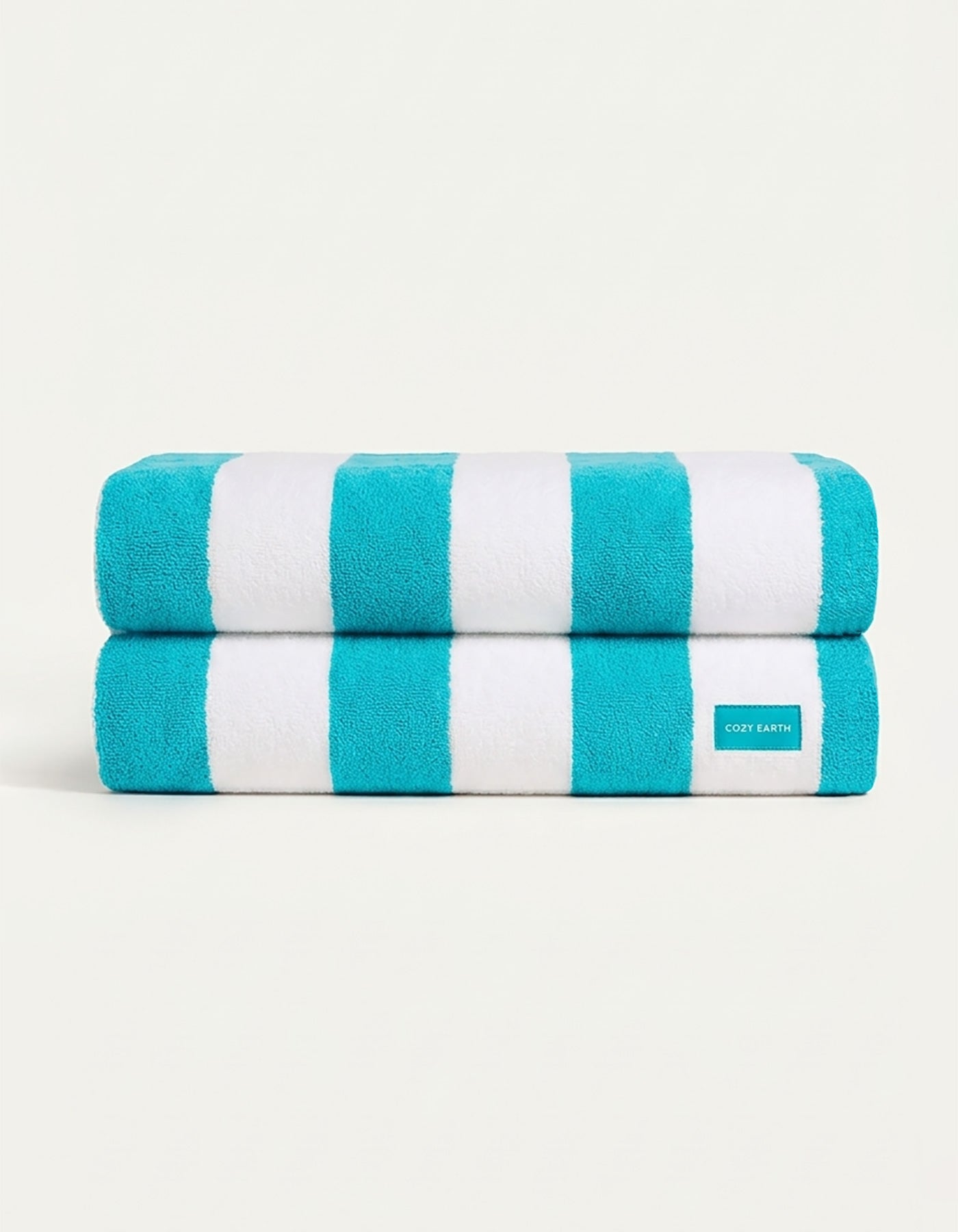 The Seaside Resort Towel Bundle by Cozy Earth features two neatly folded towels with bold turquoise and white stripes, stacked on a plain light background. A small Cozy Earth fabric label is visible on the lower towel.