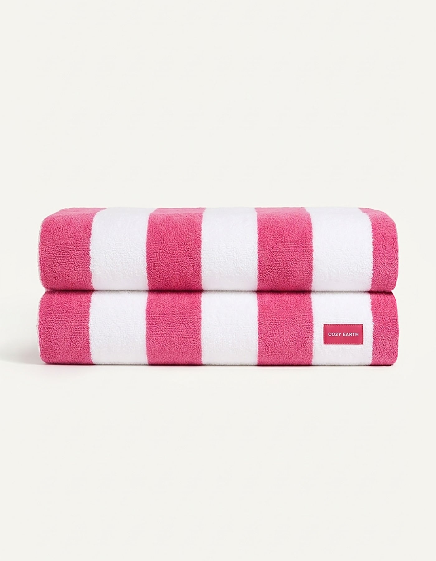 Two neatly folded towels from the Seaside Resort Towel Bundle by Cozy Earth, featuring wide pink and white stripes, are stacked together. A small white tag with red "COZY EARTH" text is visible on the bottom towel.