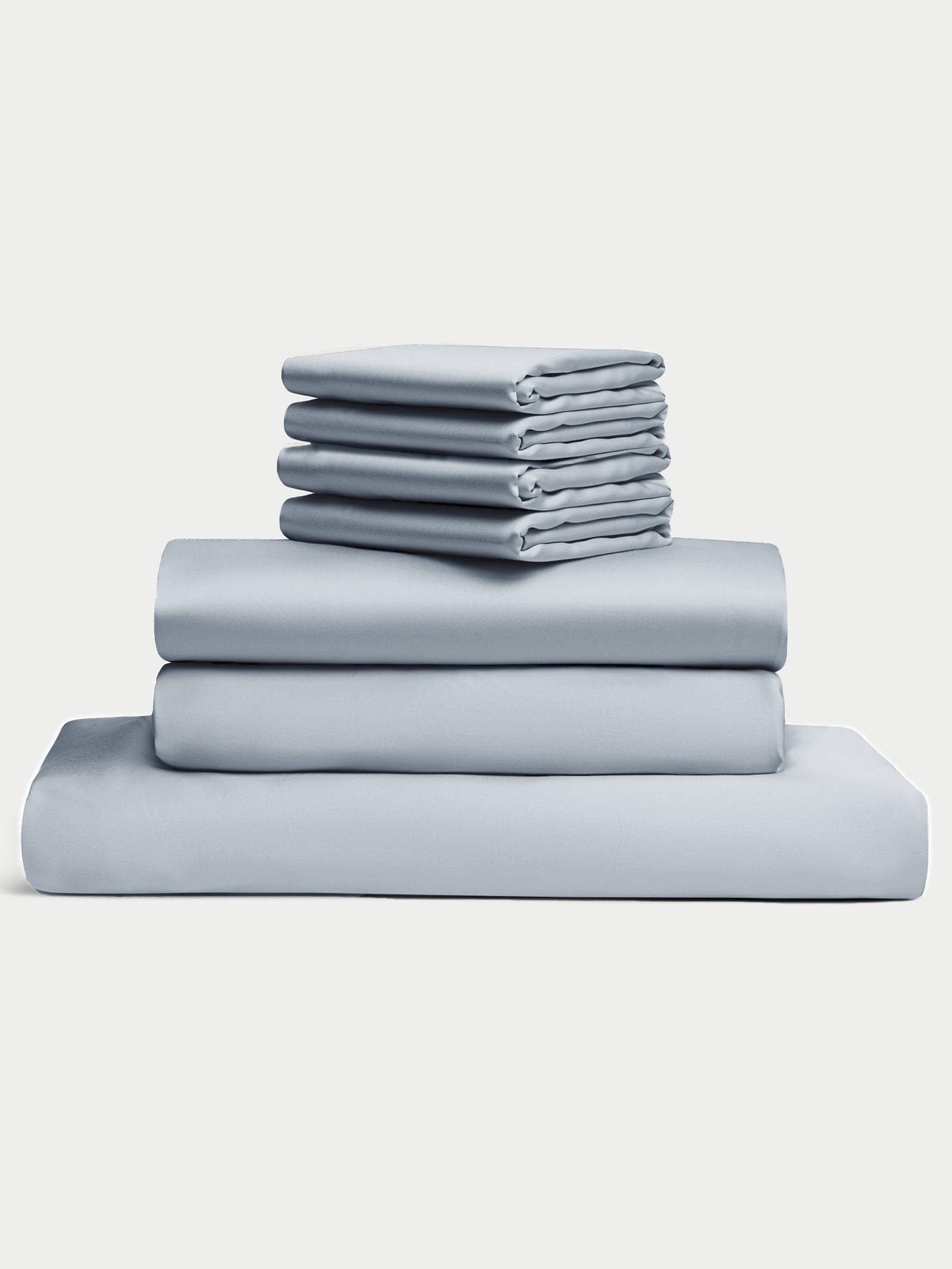 The Bamboo Bedding Core Bundle by Cozy Earth features a stack of neatly folded light blue sheets, including two larger sheets, a pillowcase, and several smaller sheets or pillowcases, all set against a white background. 