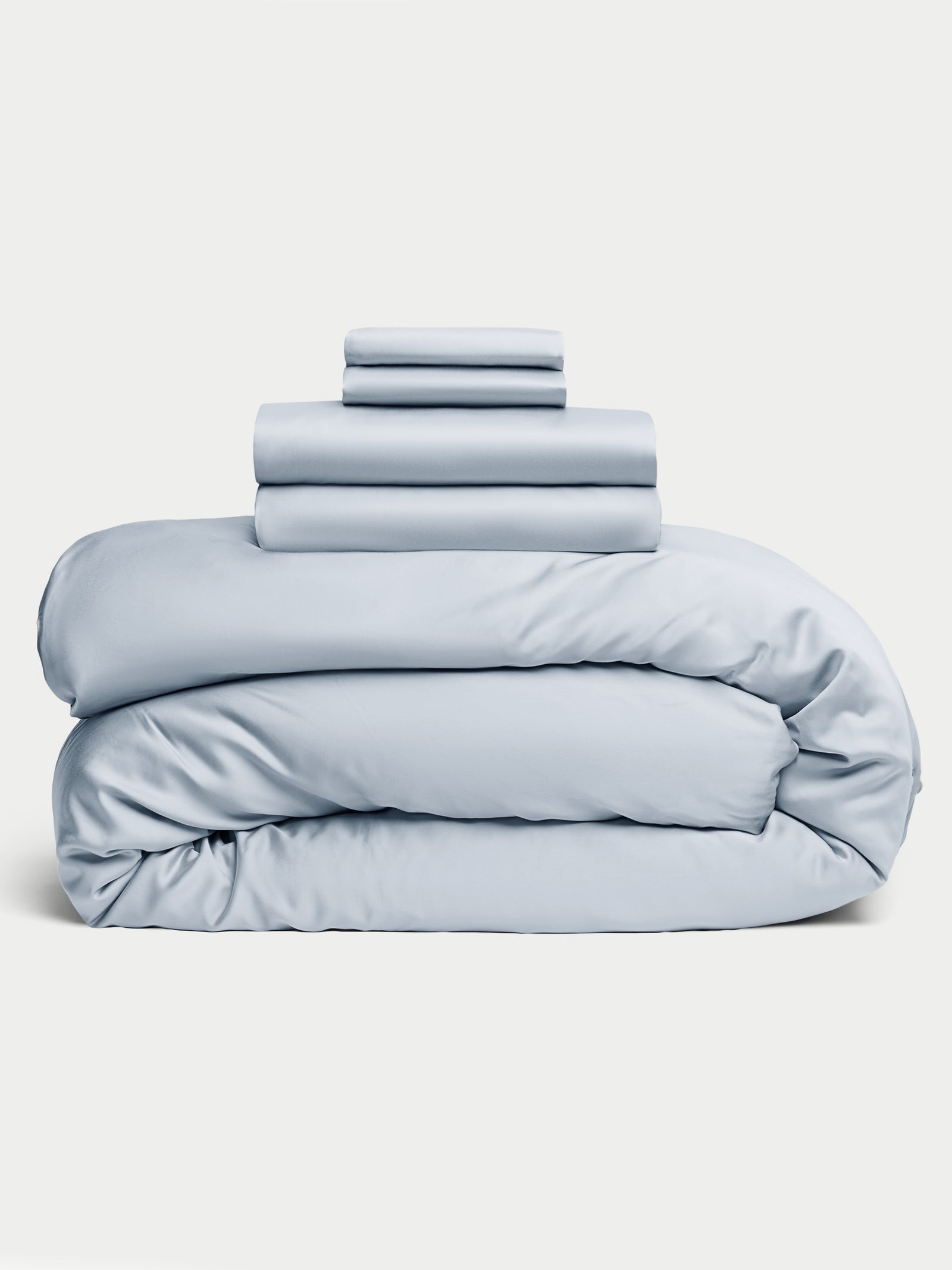 A neatly stacked set of the Bamboo Bedding Deluxe Bundle from Cozy Earth, featuring folded light blue duvet and sheets, arranged on a plain white background. 