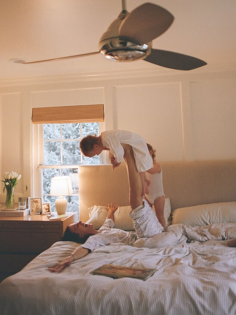 Two children playing on a bed in a bedroom with a ceiling fan.