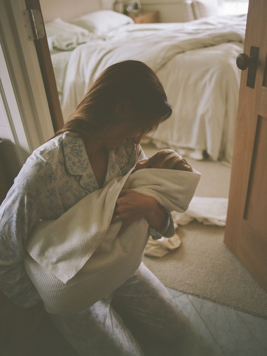 Woman sitting on a bed holding a blanket in a softly lit bedroom.