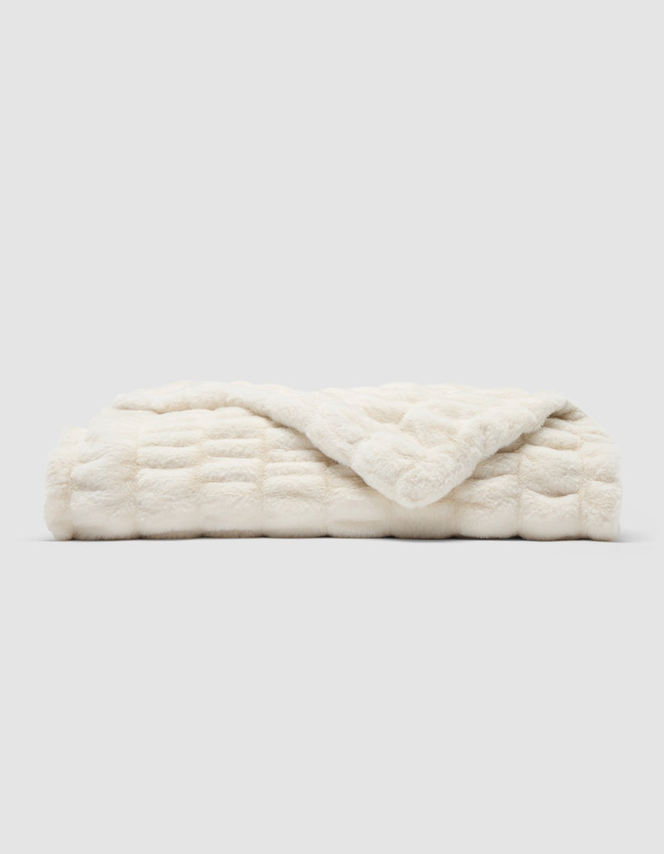 Folded cream-colored Snuggle Cuddle Blanket made of faux fur with a quilted texture.|Color:Creme