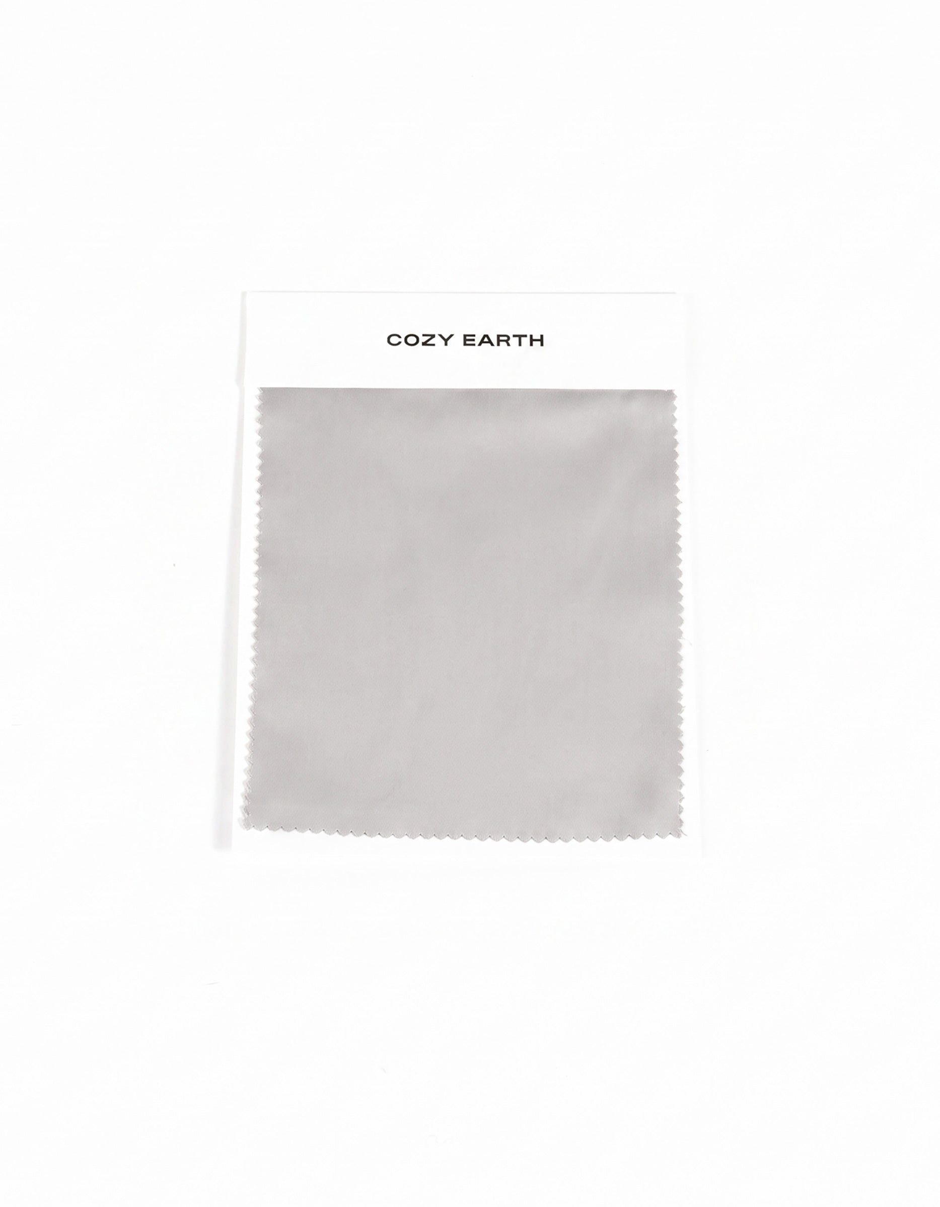 A gray Soft-Wash Cotton Sheet swatch with zigzag edges is attached to a white card labeled "Cozy Earth" at the top, displayed on a plain white background.