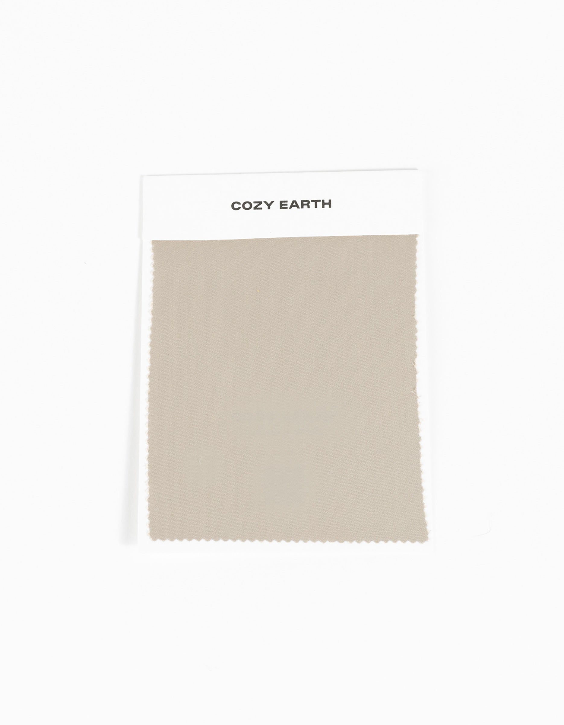 A rectangular beige Soft-Wash Cotton Sheet Swatch from Cozy Earth is attached to a white card labeled with the brand name and displayed against a plain white background.