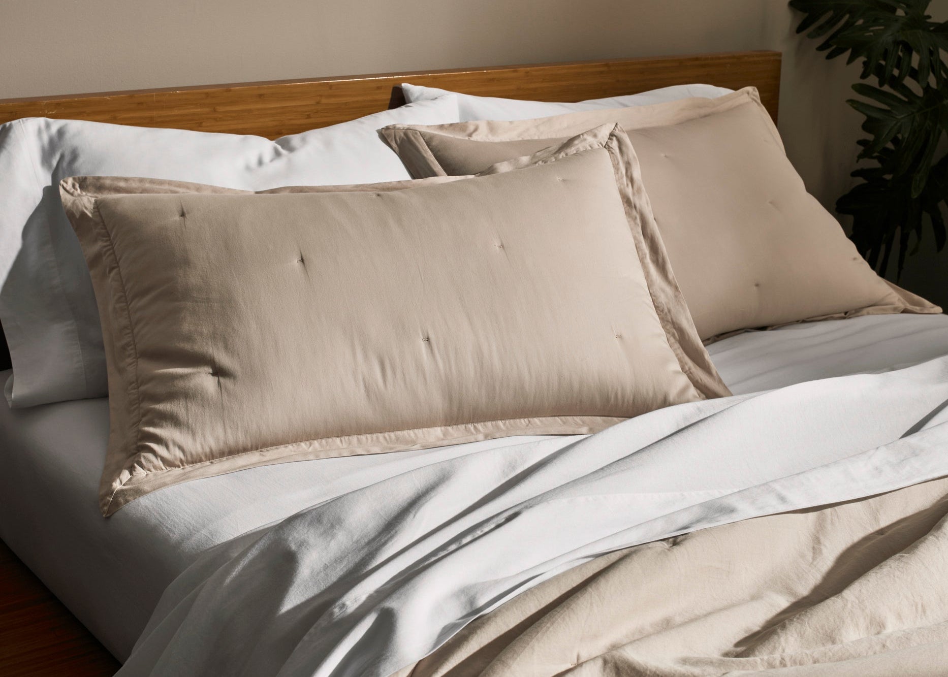 Neatly made bed with beige and white bedding against a plain wall.