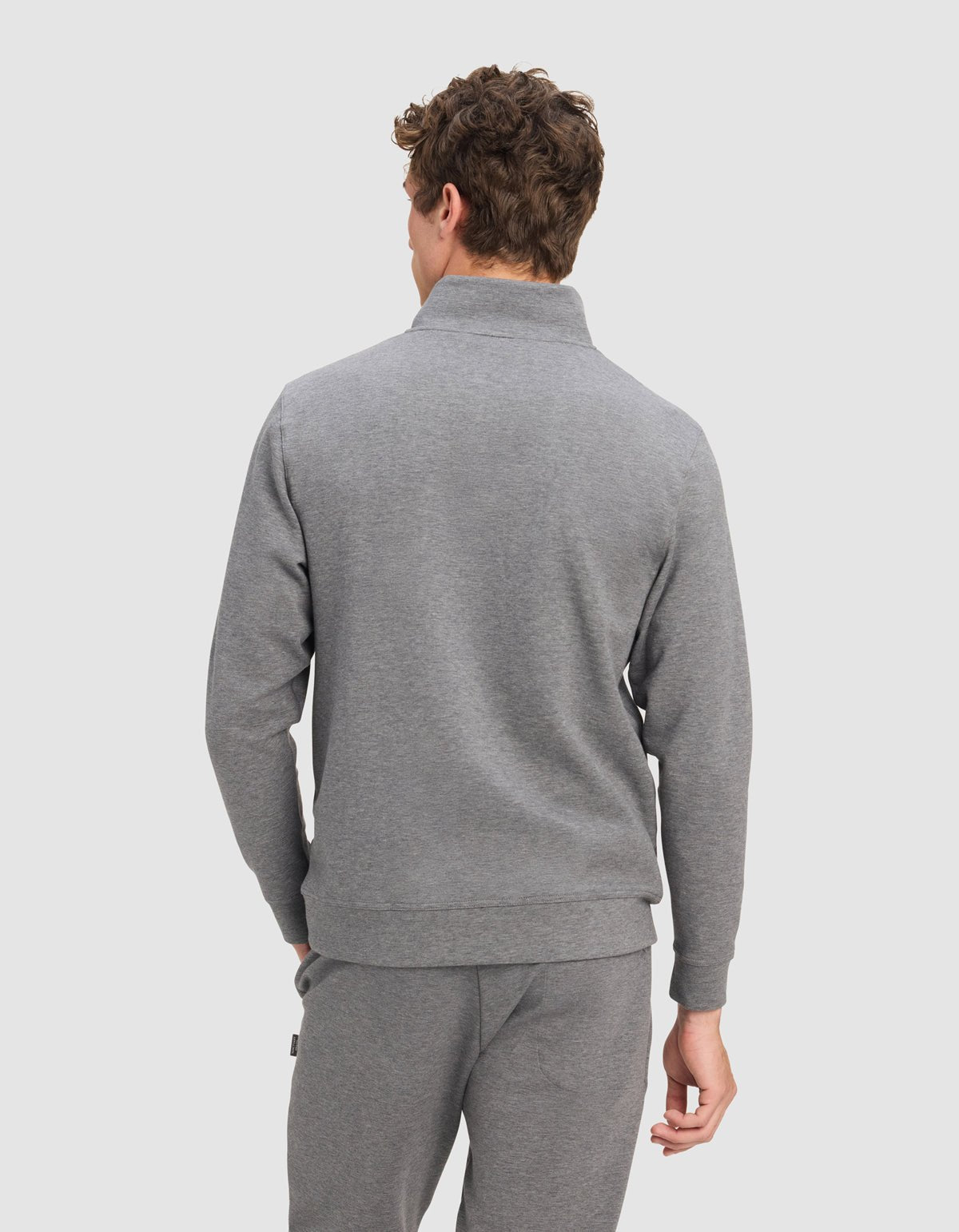 A man with curly brown hair, shown from the back against a light gray background, wears the Cozy Earth Men's StretchTech Quarter Zip in light gray.|Color:Coal Heather