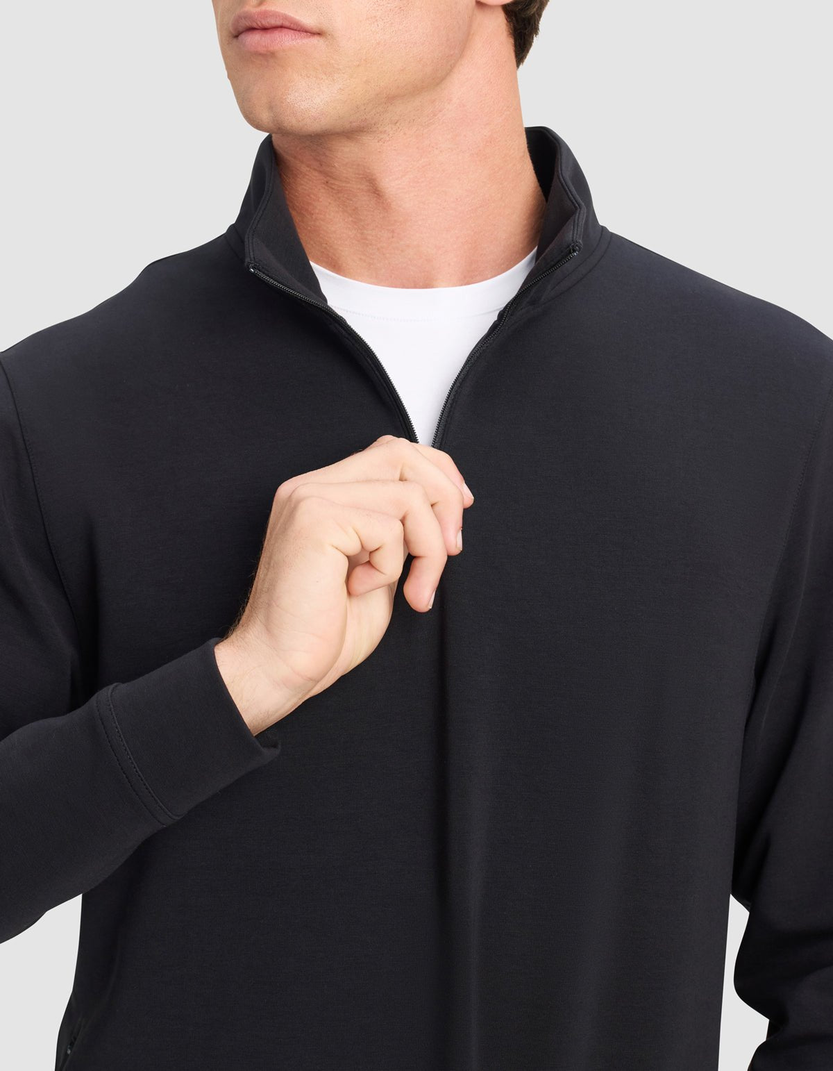 A person is shown unzipping the collar of a Cozy Earth Men's StretchTech Quarter Zip, worn over a white shirt, with their face partially visible against a plain light gray background.