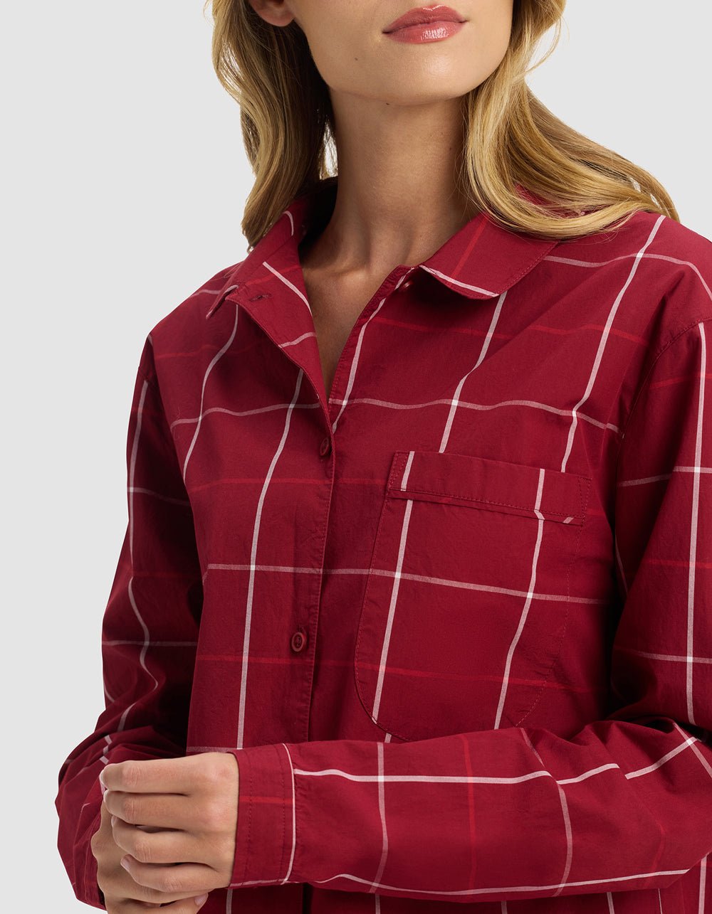 A woman models the Women's Sutton Long Sleeve Pajama Top by Cozy Earth, featuring a red and white plaid pattern and button-up front. The image is cropped at her shoulders and upper chest against a plain background.