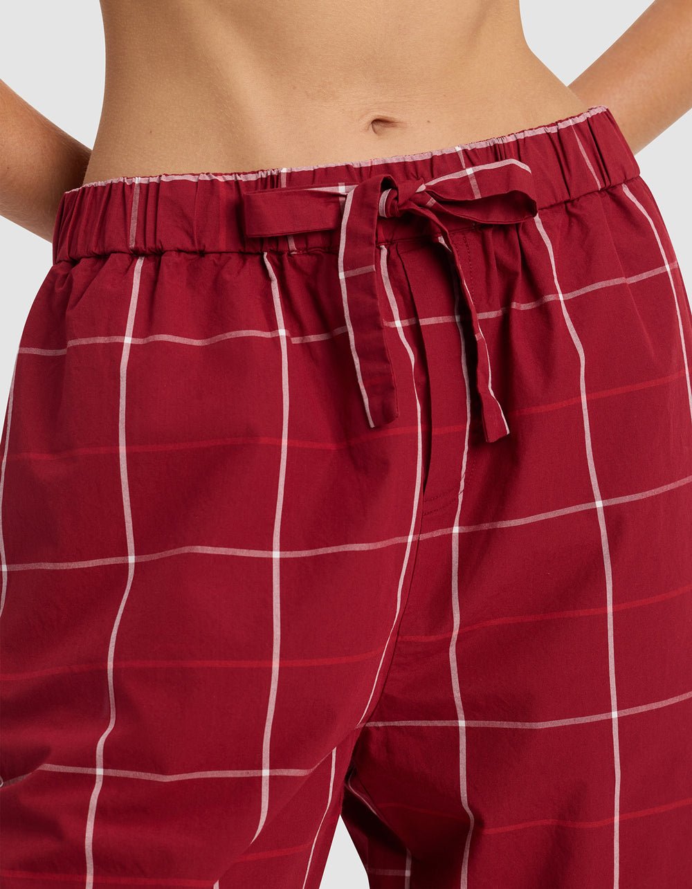A close-up of the Cozy Earth Women's Sutton Long Sleeve Pajama Set shows red plaid pants with a white grid pattern and fabric waist tie, pictured from waist to mid-thigh.