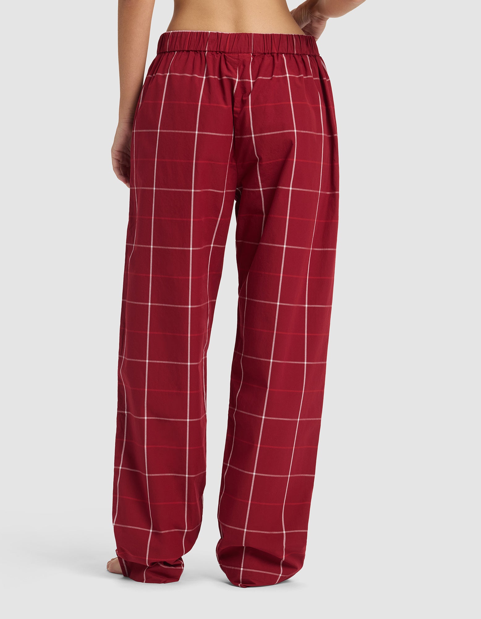 A person wearing Cozy Earth's Sutton Pajama Pant in loose-fitting red plaid with an elastic waistband, shown from the back against a plain light gray background.