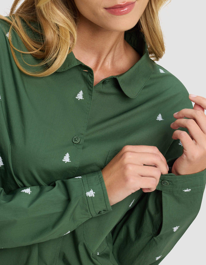 A woman, shown from the lower face down, adjusts her sleeve while wearing the Cozy Earth Women's Sutton Long Sleeve Pajama Top in green with small white tree patterns.