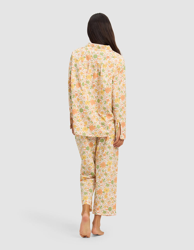 A woman stands barefoot, facing away, wearing the Cozy Earth Women's Sutton Long Sleeve Pajama Set in a pastel floral print with long sleeves and full-length pants, set against a plain light background.