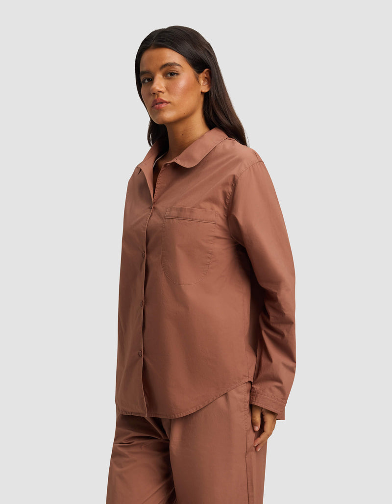 A woman with long dark hair wears the Cozy Earth Women's Sutton Long Sleeve Pajama Top in dusty rose, paired with matching pants, standing against a plain light gray background.