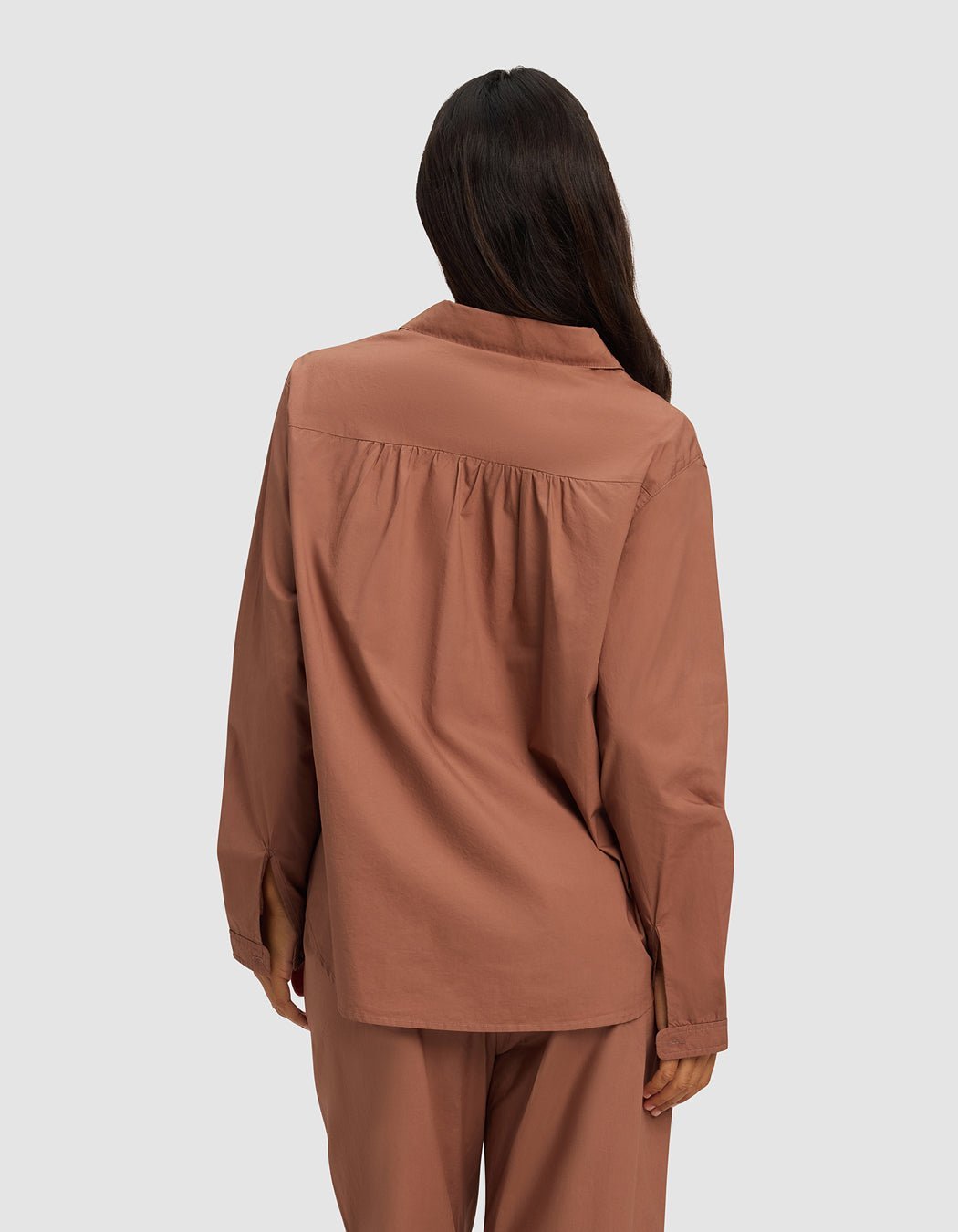 A woman with long dark hair is seen from behind, wearing the Cozy Earth Women's Sutton Long Sleeve Pajama Top in dusty rose with matching bottoms, set against a plain light gray background.