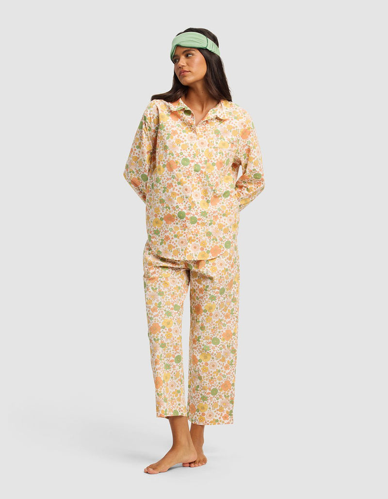 A woman stands barefoot on a plain background, hands behind her back and looking to the side, wearing the Cozy Earth Women's Sutton Long Sleeve Pajama Top and a light green sleep mask.