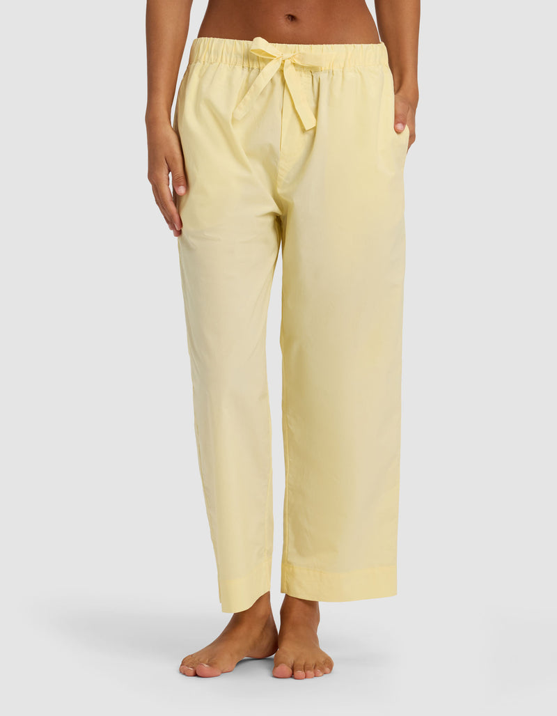 A person stands barefoot against a plain background wearing Cozy Earth Women's Sutton Cropped Pajama Pant in light yellow, featuring a loose fit, drawstring waist, and side pockets.