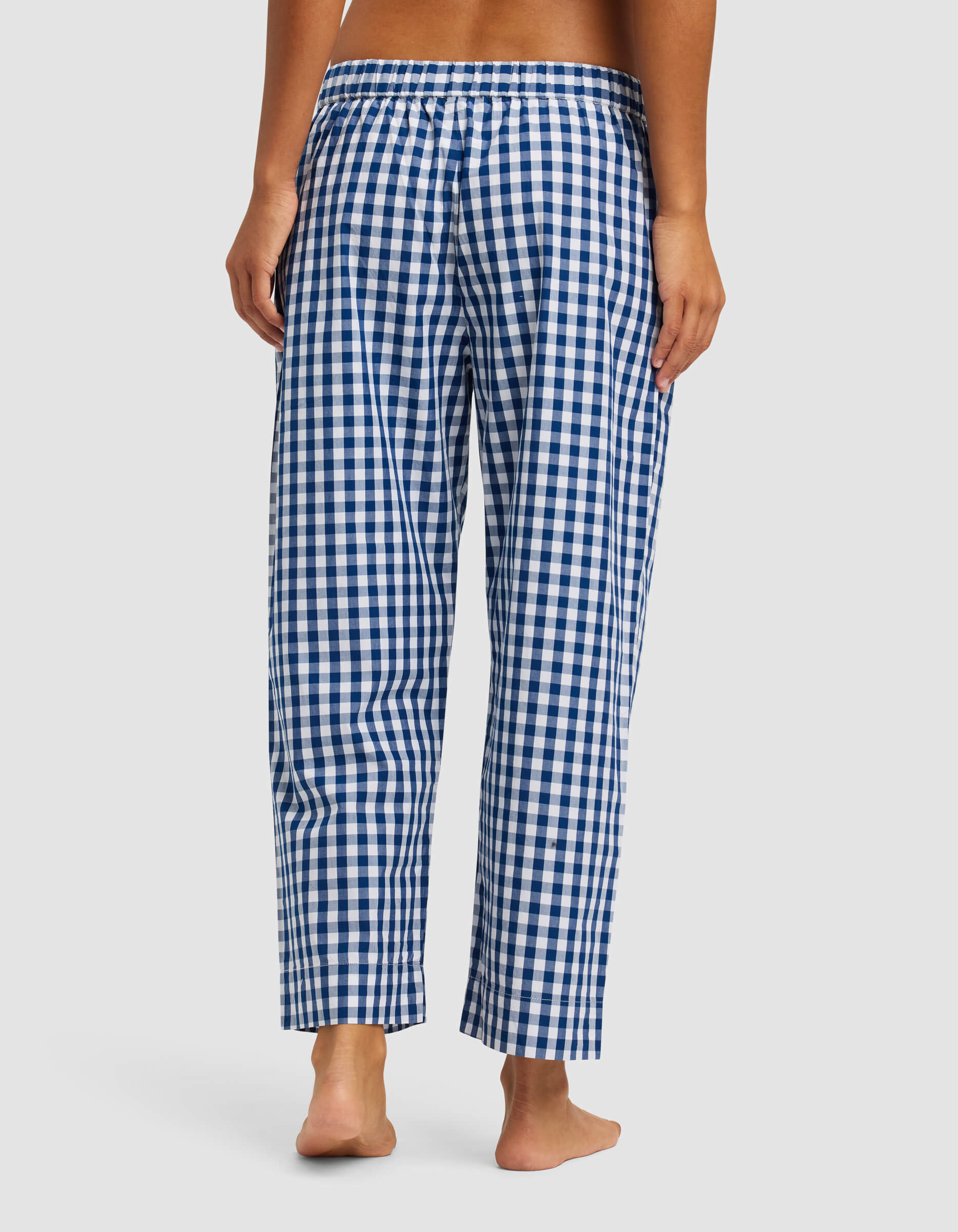 A woman stands barefoot, seen from behind, wearing Cozy Earth’s Women's Sutton Cropped Pajama Pant in blue and white check with an elastic waistband.|Color:Pacific Gingham