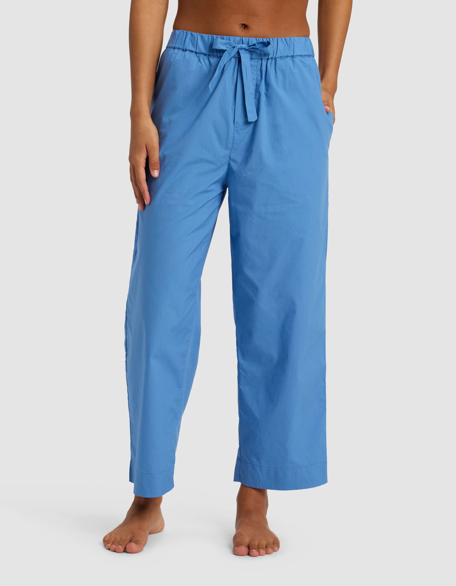 A woman wearing Cozy Earth's Women's Sutton Cropped Pajama Pant, featuring a drawstring waist and pockets in light blue, stands barefoot against a plain white background.|Color:Sailor