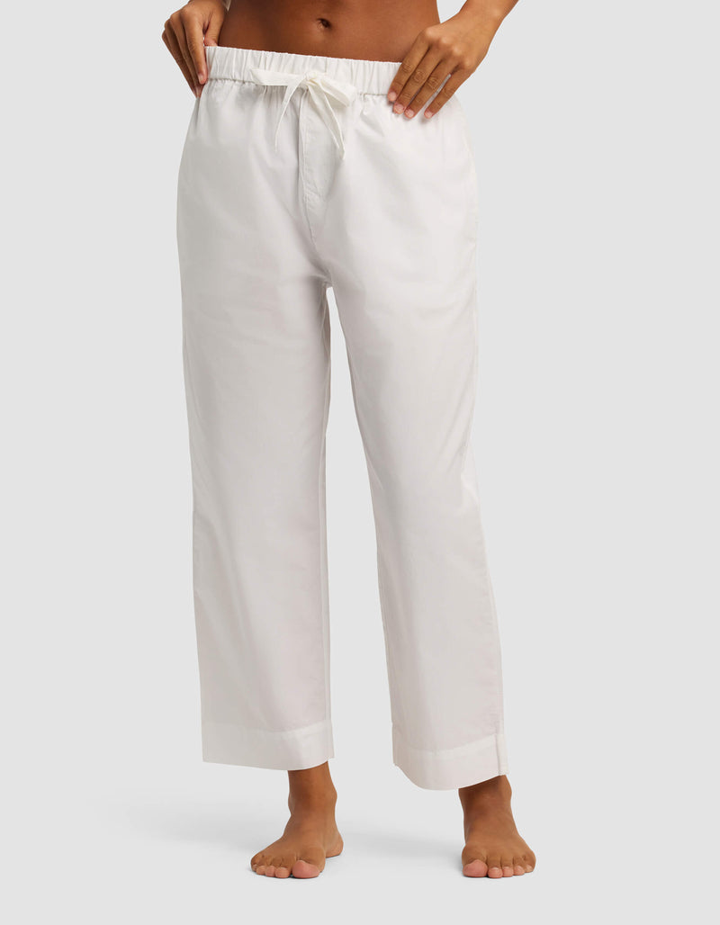 A person stands barefoot against a plain light gray background, wearing Cozy Earth’s Women's Sutton Cropped Pajama Pant—loose-fitting with a white drawstring and cropped just above the ankles.